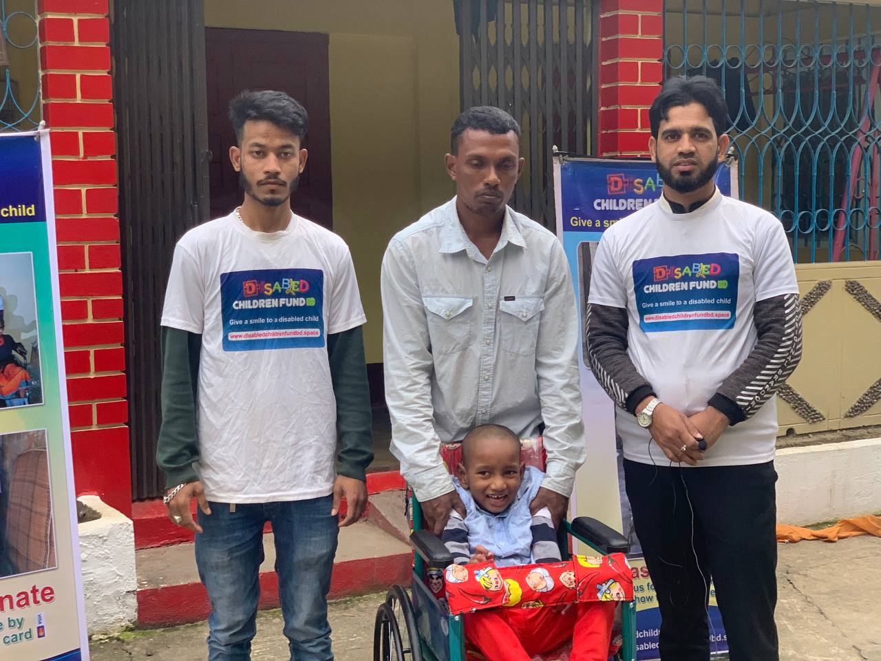 Disabled Children Fund team with a child in a new wheelchair, photographed outside a building in Sylhet
